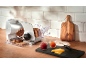 Electric slicer with bread, cheese, and jams on a wooden countertop.