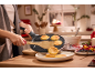 A person cooking mini pancakes in a special pan, serving them on a plate with berries.