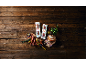 Sausages in packaging and on a board, with bread, mustard, and herbs on a wooden table.