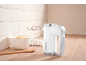 White hand mixer with dough hooks on a wooden counter next to a bowl of flour and eggs.