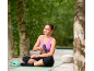 Woman sitting on a yoga mat with a massage gun, smiling.