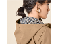 Woman in a beige hooded raincoat with a patterned lining, wearing gold hoop earrings.