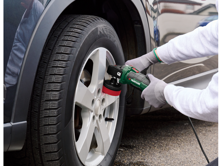 Person polishing a car wheel rim with an electric tool.