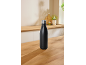 Black insulated bottle on a wooden kitchen counter with blurred background.
