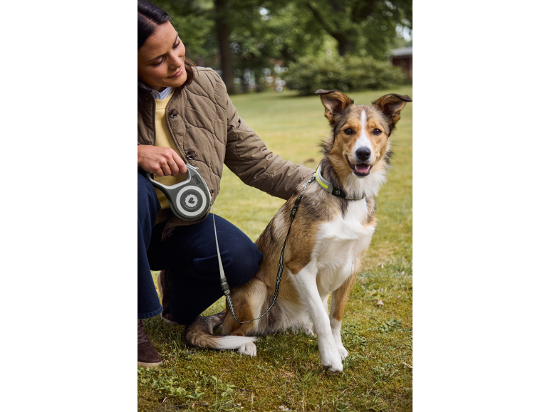 Woman with dog on a retractable leash and collar, on a green lawn.