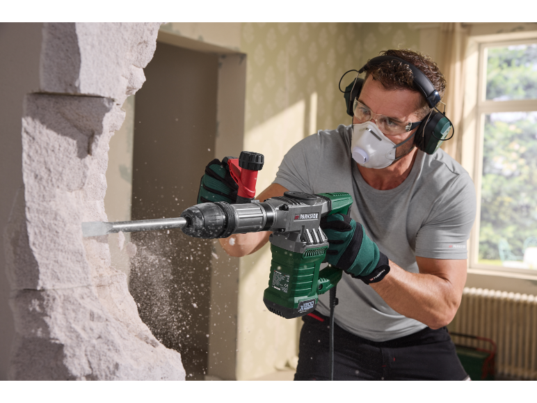 Man using a demolition hammer to break down a wall, wearing protective gear.