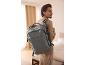 Man with a grey backpack on his back, looking to the right in a bright room.