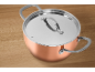 Copper pot with a metal lid and handles on a wooden table.