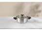 Stainless steel pot with a glass lid on a white marble table.