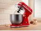 Red kitchen stand mixer with stainless steel bowl, eggs, and baking ingredients.