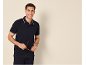 Man in navy polo shirt and trousers, holding sunglasses, smiling.