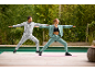 Two people in tracksuits doing yoga outdoors by a pool.