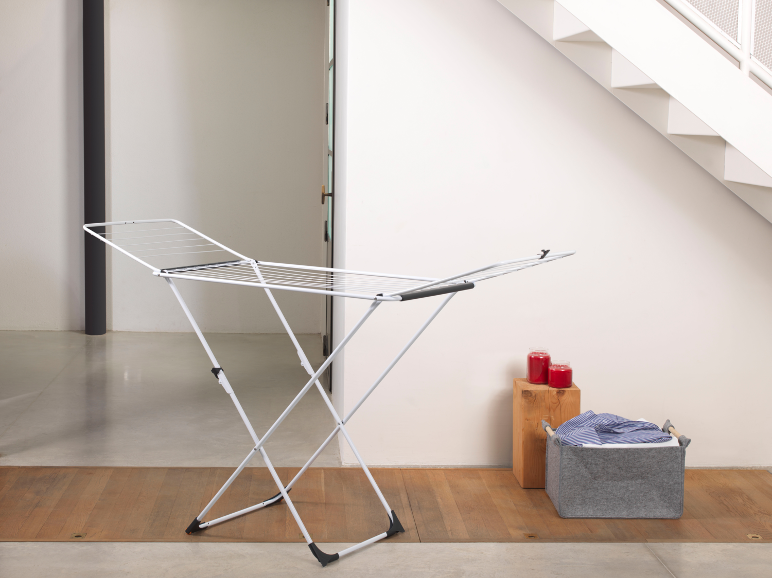 White clothes drying rack with laundry basket and red candles in a modern interior.