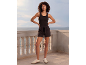 Woman in black tank top and black shorts, with a sea view.