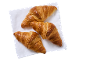 Three golden-brown croissants on a white napkin, viewed from above.