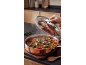 Person lifting lid from steaming vegetable dish in a copper pot.