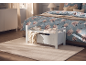 White wooden storage bench with blanket and books, next to a bed with floral bedding.