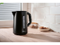 Black electric kettle on a wooden countertop with white tiles and cookies.