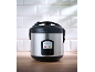 Stainless steel rice cooker with a black lid, with steam escaping from the top.