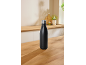 Black insulated bottle on a wooden kitchen counter with blurred background.