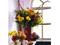 Autumn flower bouquet with gerberas, roses, and chrysanthemums in a red vase, with fruits and vegetables.