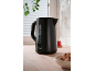 Black electric kettle on a wooden countertop with tea and cookies.