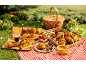 A picnic with a basket, croissants, pastries, berries, and drinks on a red checkered tablecloth.