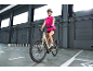 Woman in a pink vest and helmet riding an electric bicycle in an indoor setting.