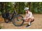 Woman checking tire pressure of an e-bike with a pannier in a forest setting.