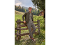 Man in khaki bomber jacket, T-shirt, and cargo pants, leaning on a wooden fence.