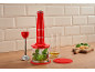 Red immersion blender with attachments, ready to make pesto on a wooden board.