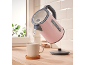 Pink kettle pouring hot water into a ceramic mug in a kitchen.