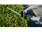 Gloved person trimming a hedge with cordless hedge shears.