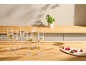 Champagne flutes with sparkling wine and raspberries on a wooden kitchen counter.