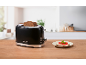 Black toaster with two slices of bread and a plate of toast on a wooden countertop.