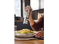 Hand seasoning a couscous dish with an electric pepper grinder.