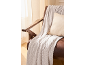 Knitted blanket and cushion on a brown armchair by a window.