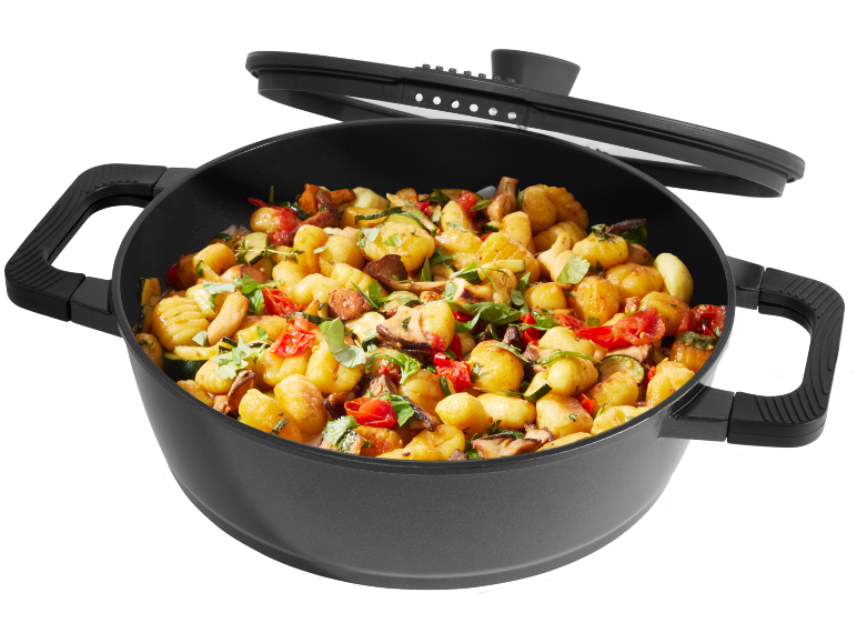 A black pot filled with gnocchi, zucchini, mushrooms, and tomatoes, with a lid resting on top.