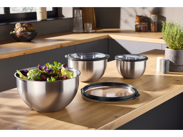 Stainless steel mixing bowls with lids, one filled with salad, on a kitchen counter.