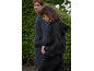 Couple in comfortable tracksuits, man in grey, woman in black, walking by a green hedge.