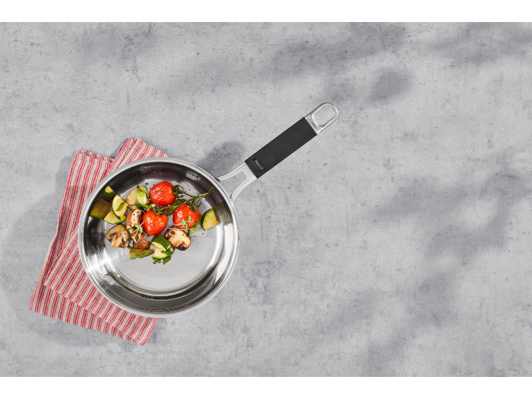 Stainless steel frying pan with roasted vegetables on a striped kitchen towel.