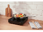 Induction hob with vegetables and seafood cooking on a wooden countertop.