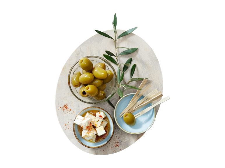 Green olives, feta cheese, and an olive branch on a wooden serving board.