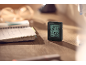 Digital thermo-hygrometer on a wooden desk next to an open notebook.