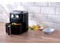 Black air fryer with fries, oil, sauces, and rosemary on a wooden table.