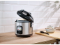 Rice cooker with cooked rice, a bowl of rice, and a spoon on a wooden counter.
