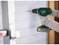 A person drilling into a white brick wall with a cordless drill.