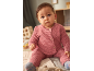 Baby in a pink knitted set, sitting on a blanket.