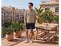 Man in khaki polo shirt and black shorts on a sunny terrace overlooking the city.