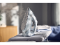 Steaming iron on an ironing board with folded laundry in the background.